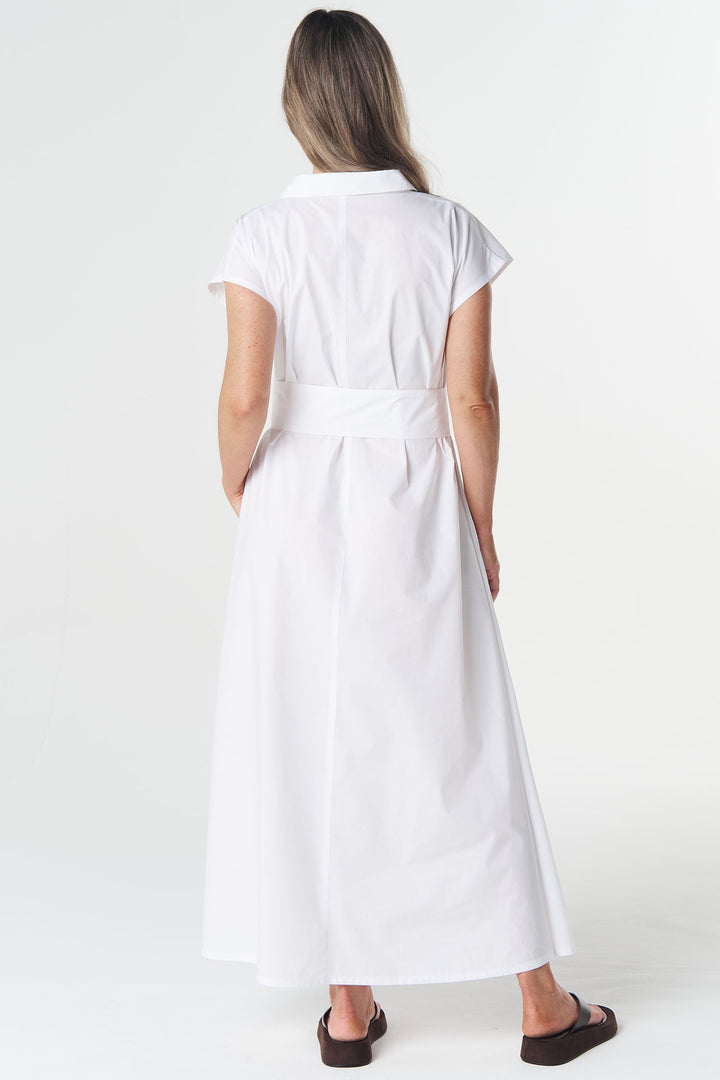 A woman viewed from behind wearing a white short-sleeve collared dress with a matching waist tie, paired with dark brown flat sandals, against a plain white studio background.