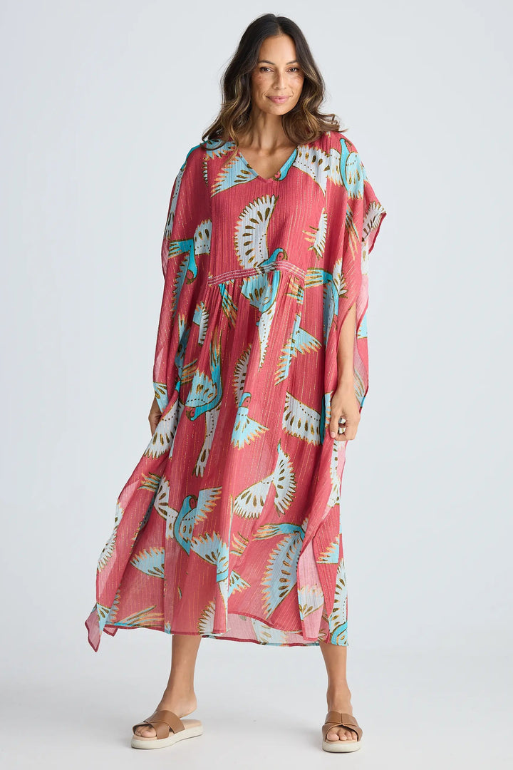 Woman wearing a pink dress with a colorful animal print on a white background. Holiday Trading Lorrini Kaftan Red Macaw