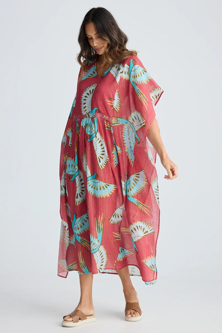 Woman wearing a pink dress with blue floral patterns on a white background. Holiday Trading Lorrini Kaftan Red Macaw