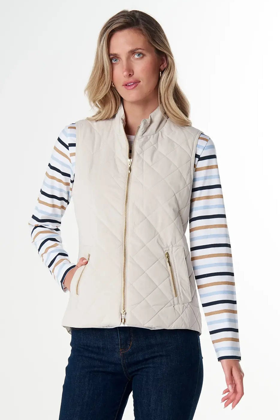 Woman wearing a beige vest, striped shirt, and dark jeans on a white background