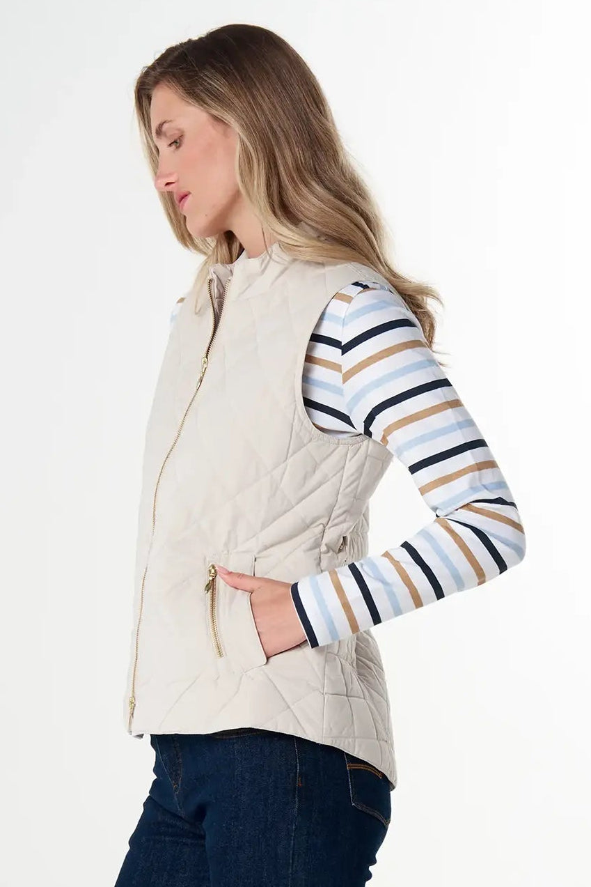 Woman wearing a beige vest, striped shirt, and dark pants on a white background
