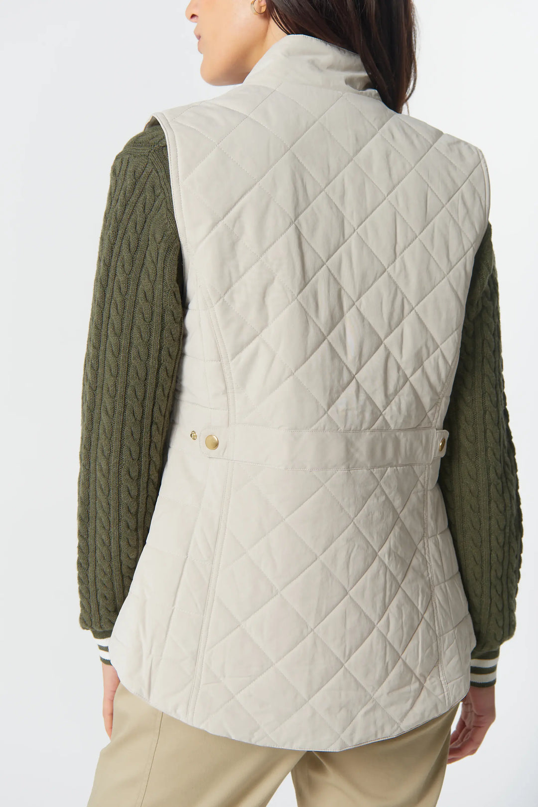Person wearing a beige quilted vest over a green sweater on a white background