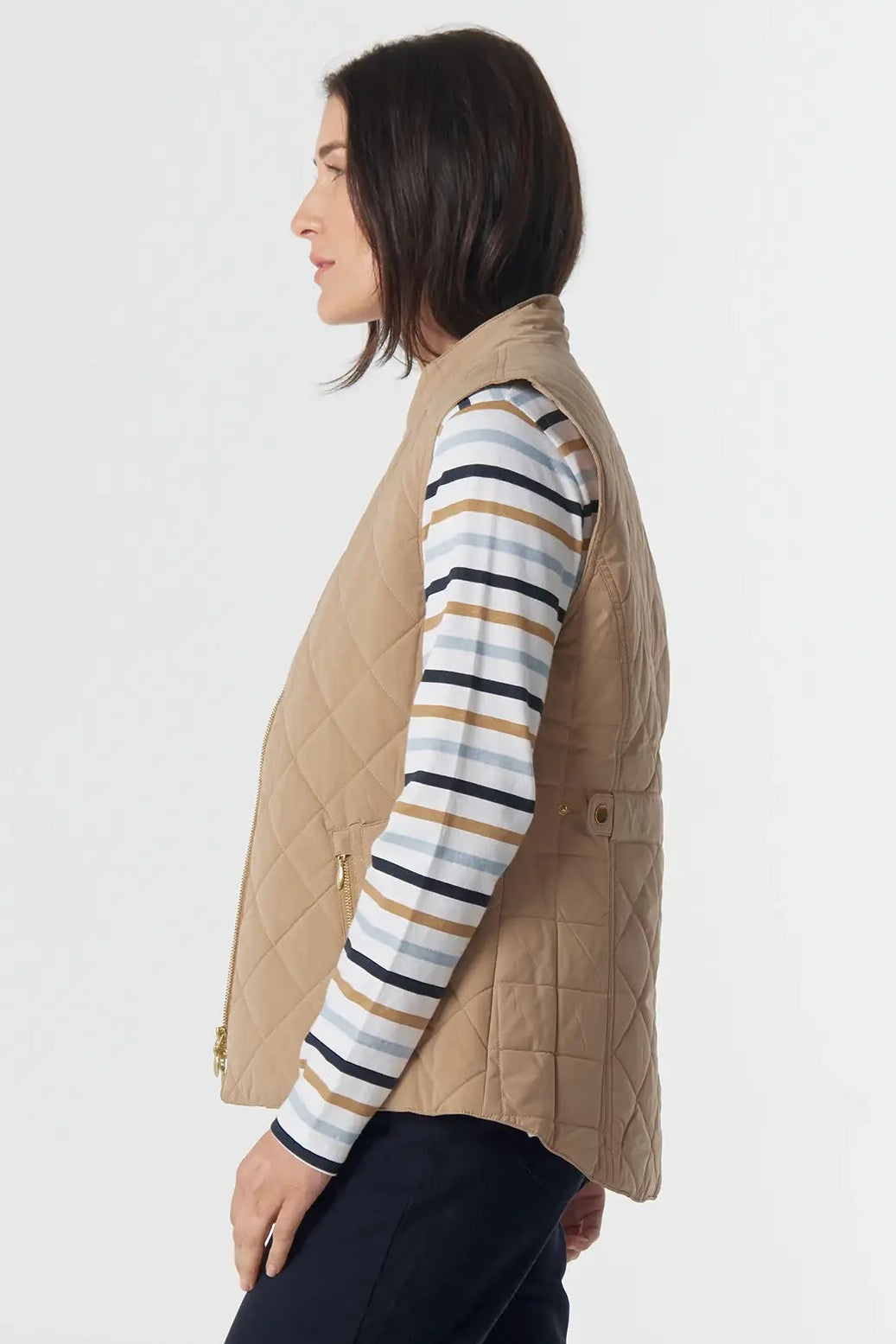Person wearing a beige vest over a striped shirt with dark pants on a white background