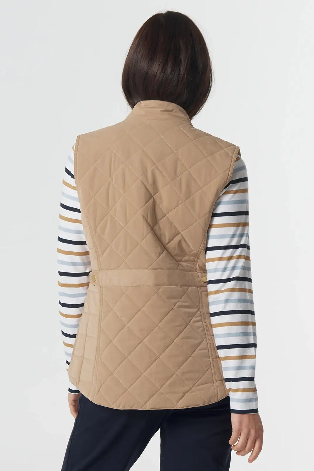 Person wearing a beige quilted vest over a striped shirt with navy pants on a white background