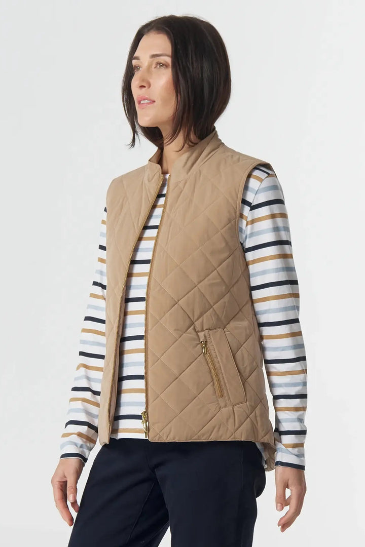 Woman wearing a beige quilted vest over a striped shirt with black pants on a white background