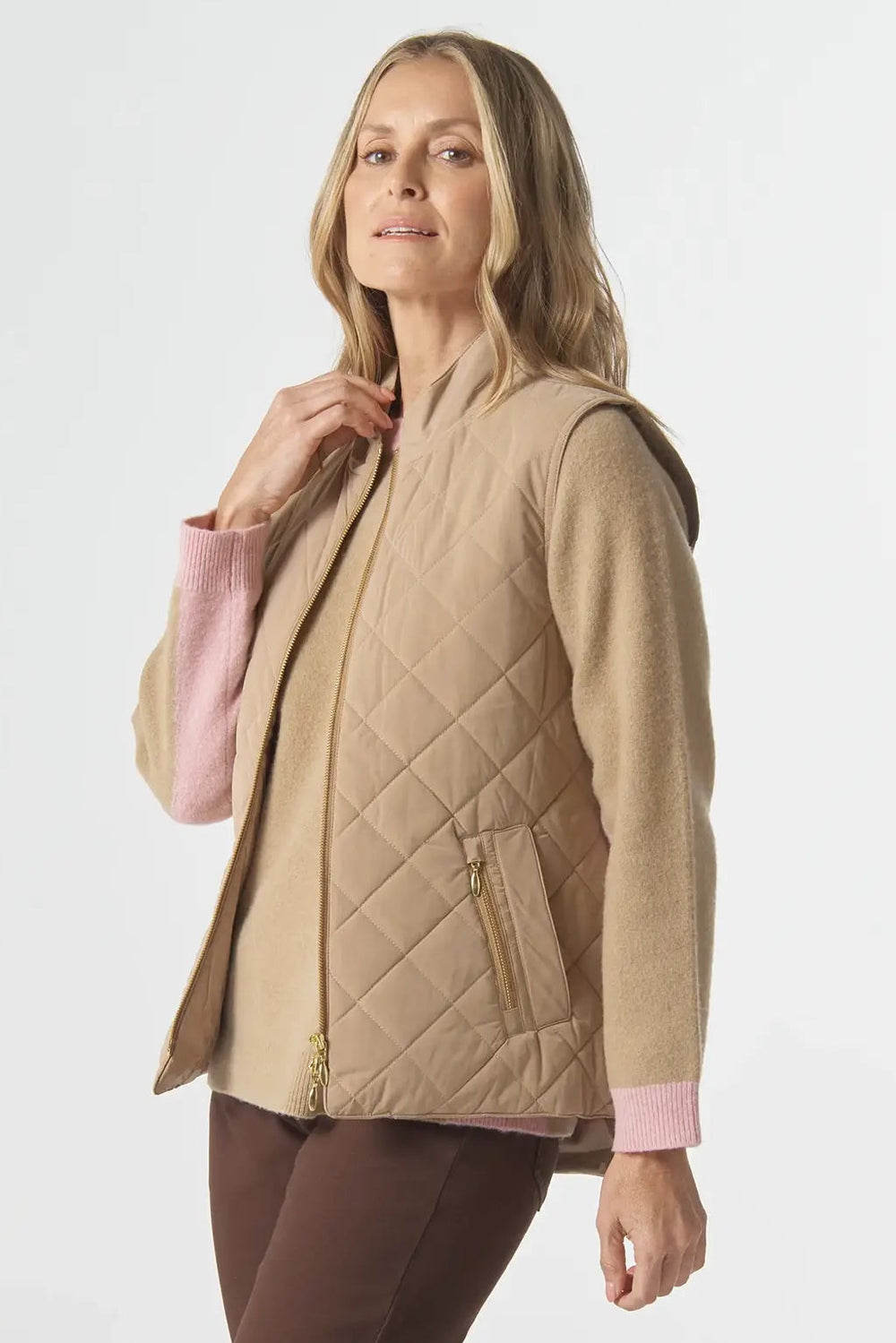 Woman wearing a beige quilted jacket and brown pants on a white background