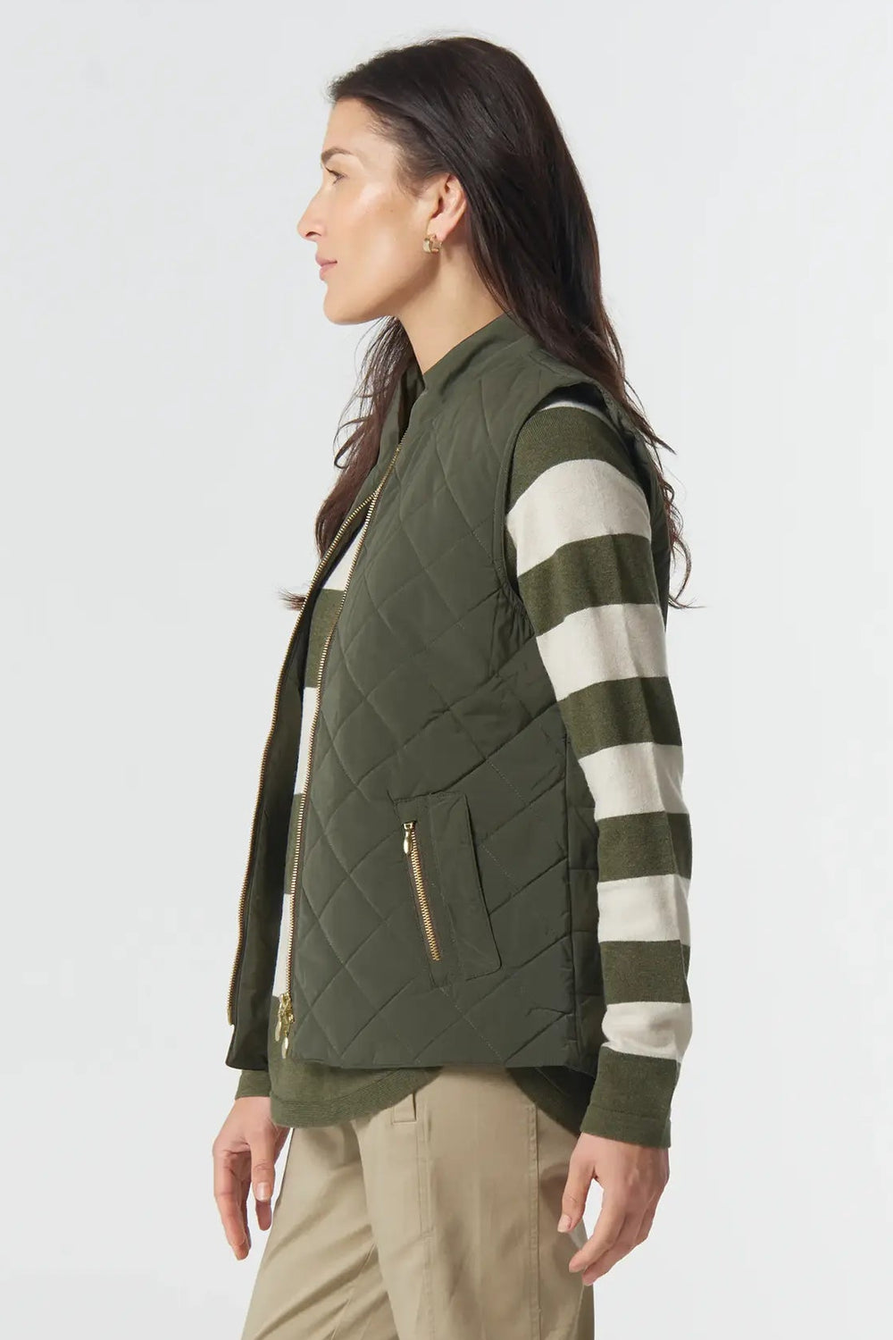 Woman wearing a green vest over a striped shirt with beige pants on a white background