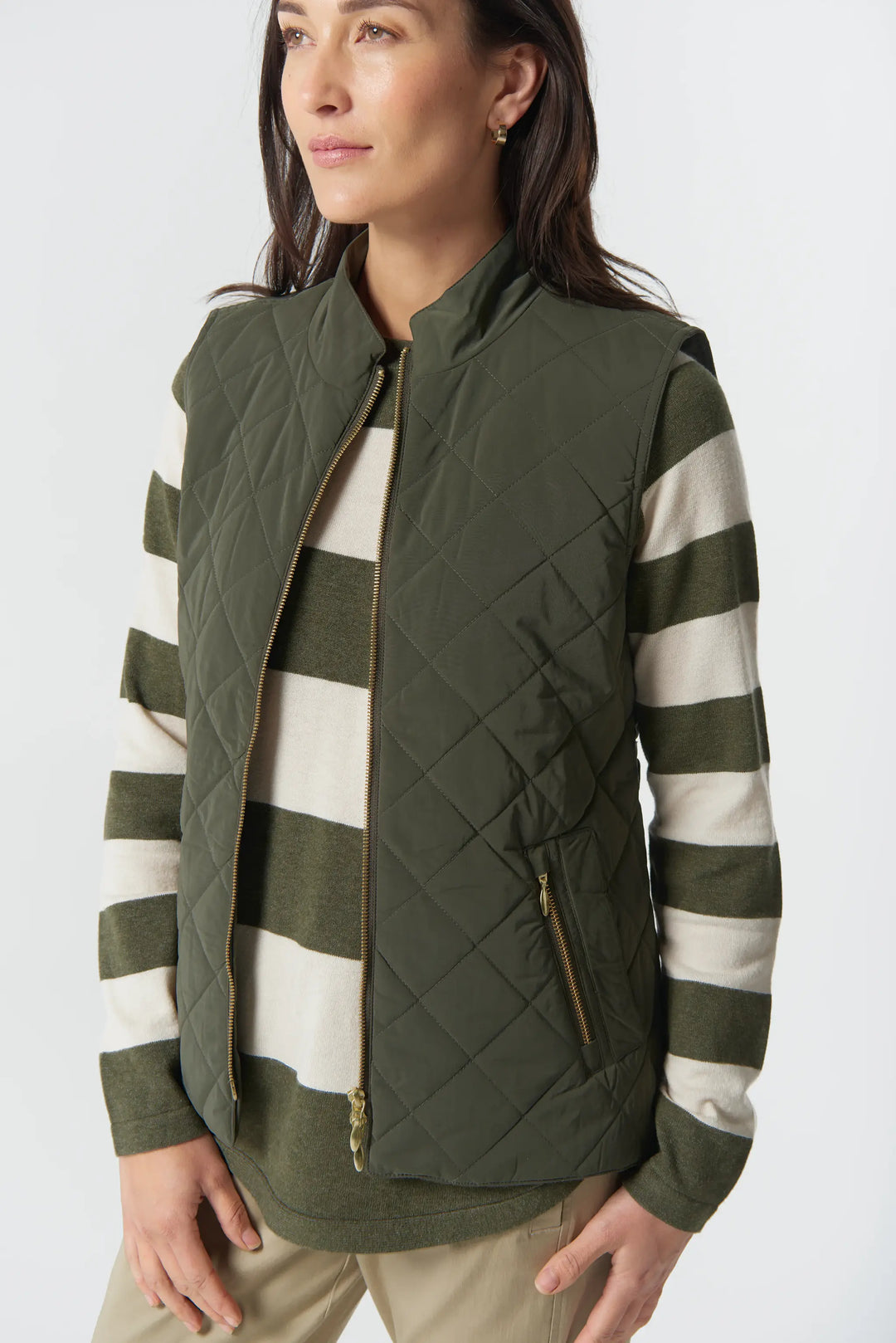 Woman wearing a green quilted vest over a striped shirt on a white background