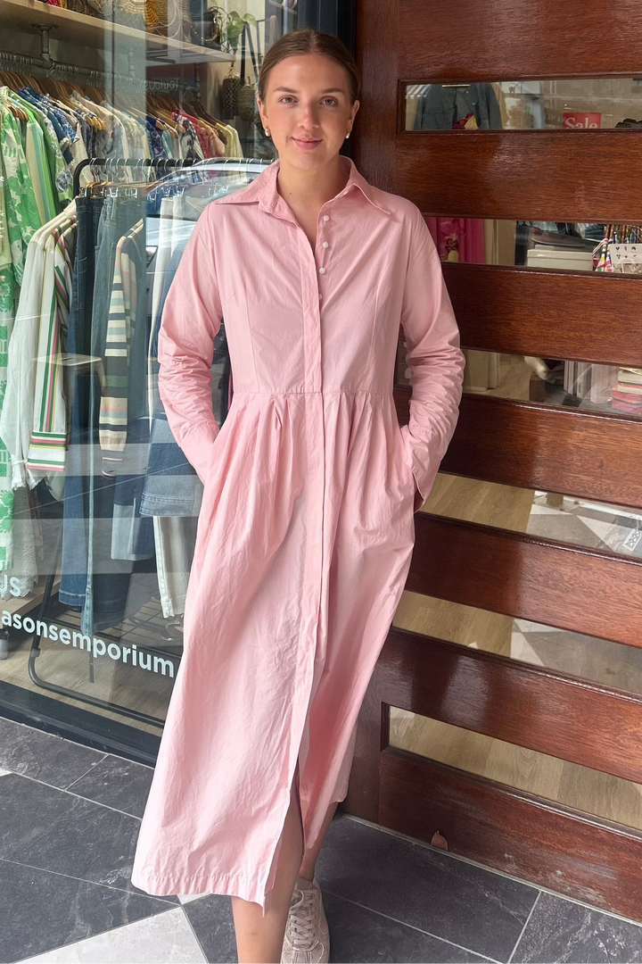 Woman in a pink dress standing in front of a store with a wooden door.