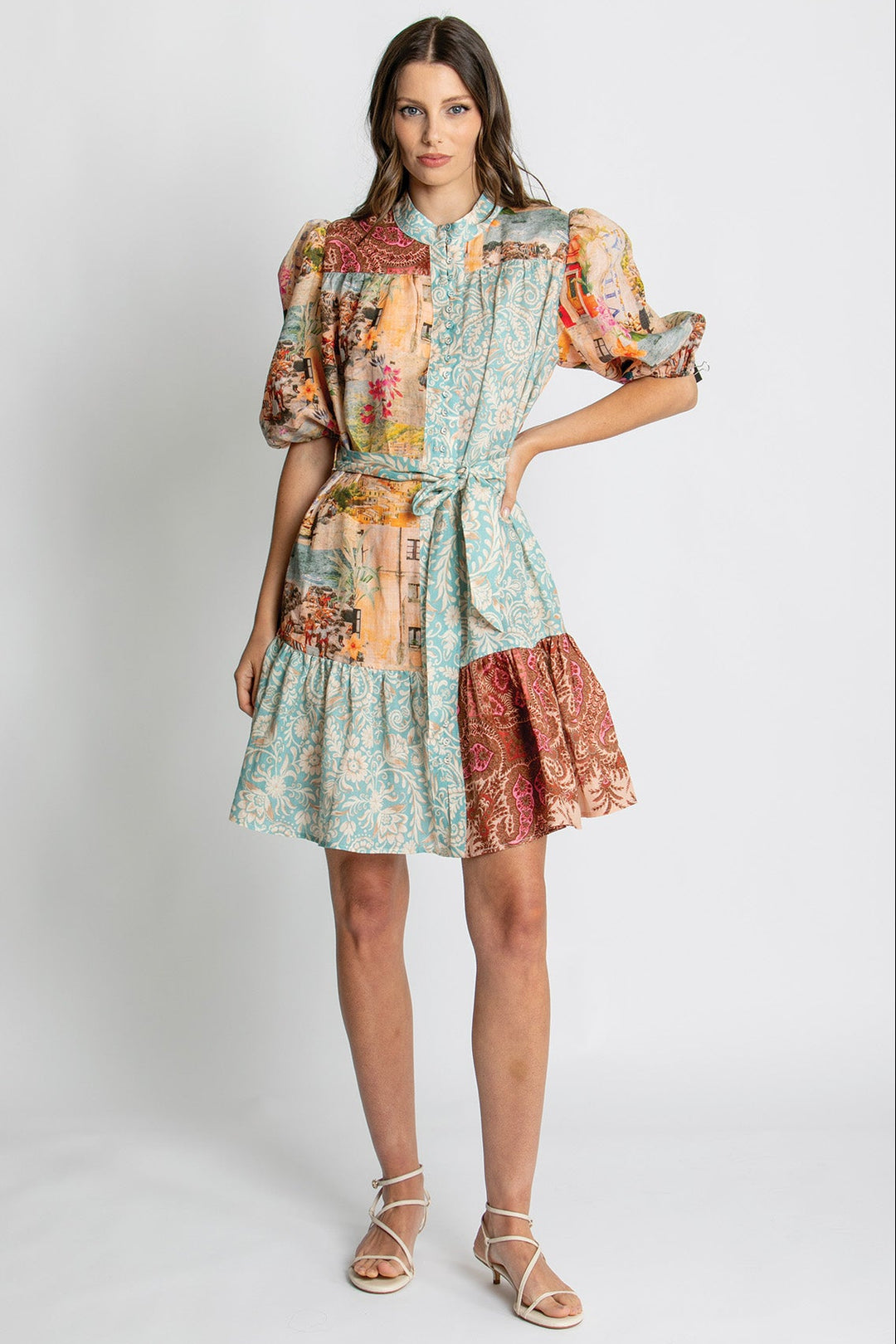 A woman modeling a short patchwork-print dress with puff sleeves, a tie waist, and a tiered skirt in a studio setting.
