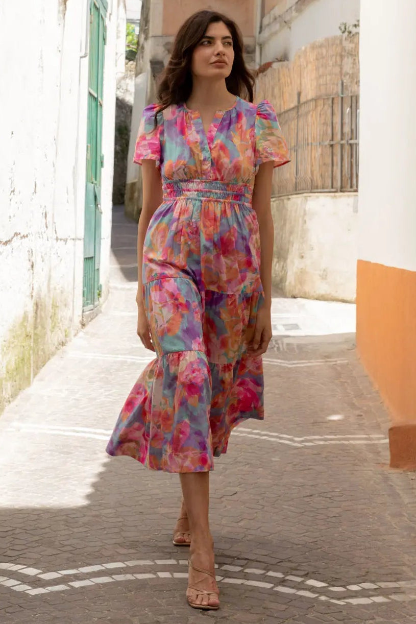 A woman standing on a street corner wearing a multicolored floral midi dress with short sleeves and a V-neck.