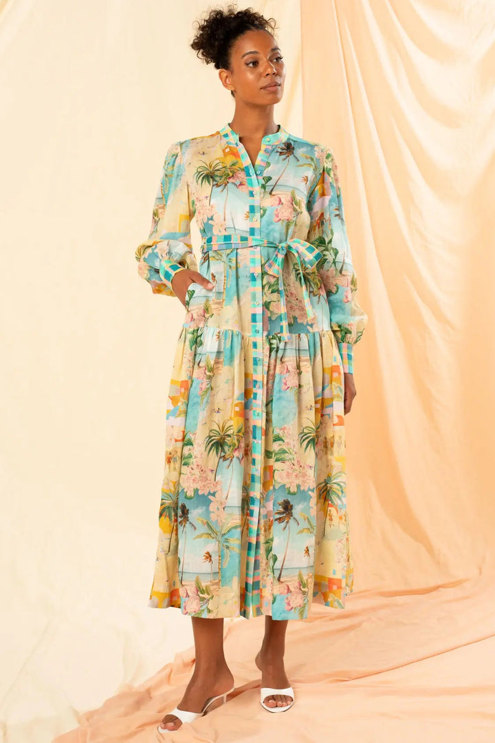 A woman standing by the sea wearing a multicolored floral maxi dress with long sleeves, a mandarin collar, and side seam pockets.