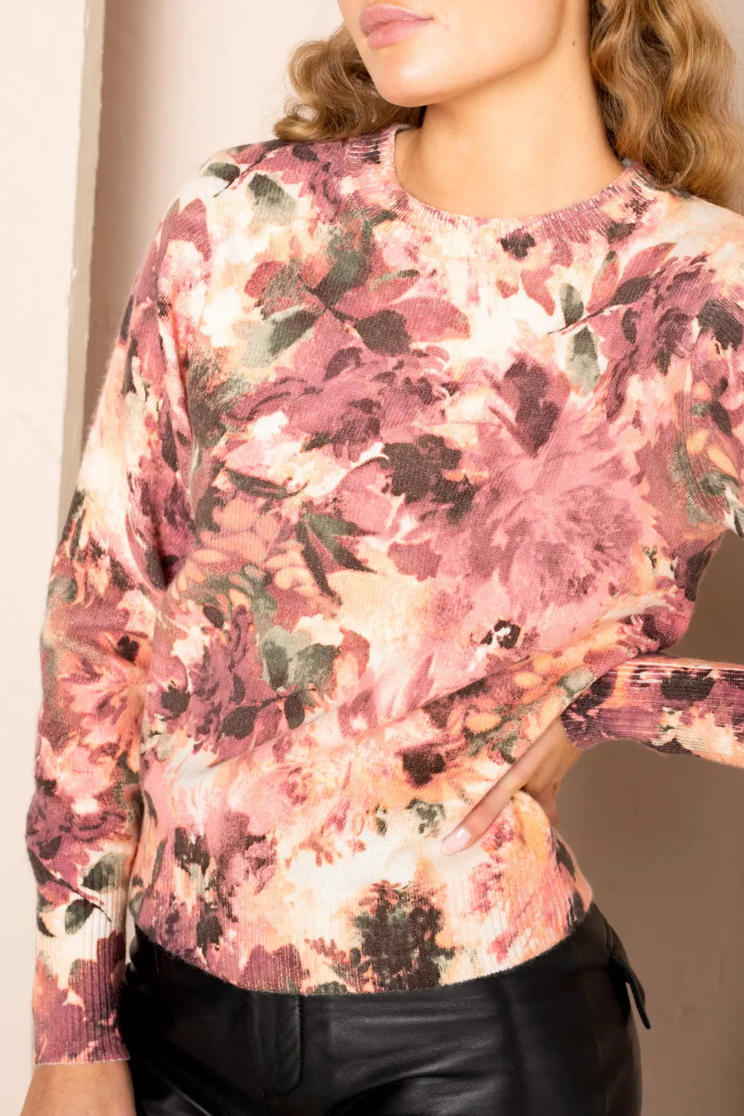 A female model wearing a long-sleeved knitted pullover with a sunset print, paired with black pants.
