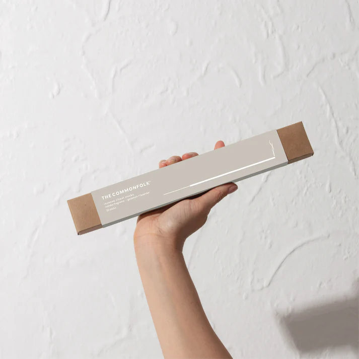 Hand holding a product box labeled 'The Commonolk' against a light background