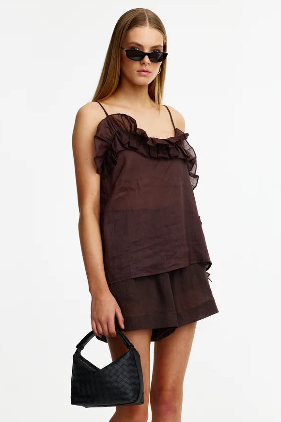 A model wearing a dark brown ruffled camisole top and matching shorts, holding a black quilted handbag, photographed against a plain white studio background.
