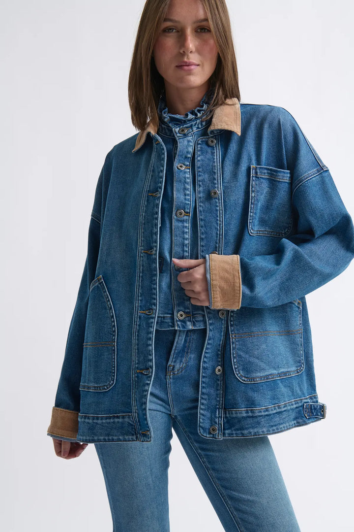 Woman wearing a blue denim jacket with brown cuffs and collar on a white background