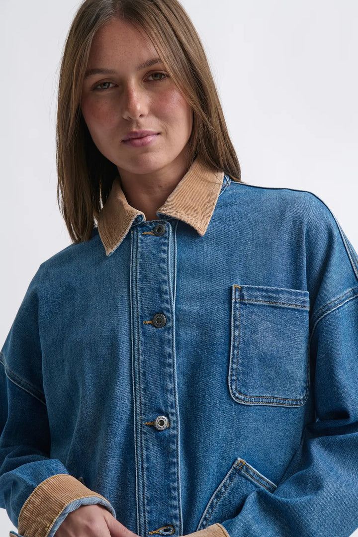 Person wearing a blue denim jacket with a beige collar on a white background