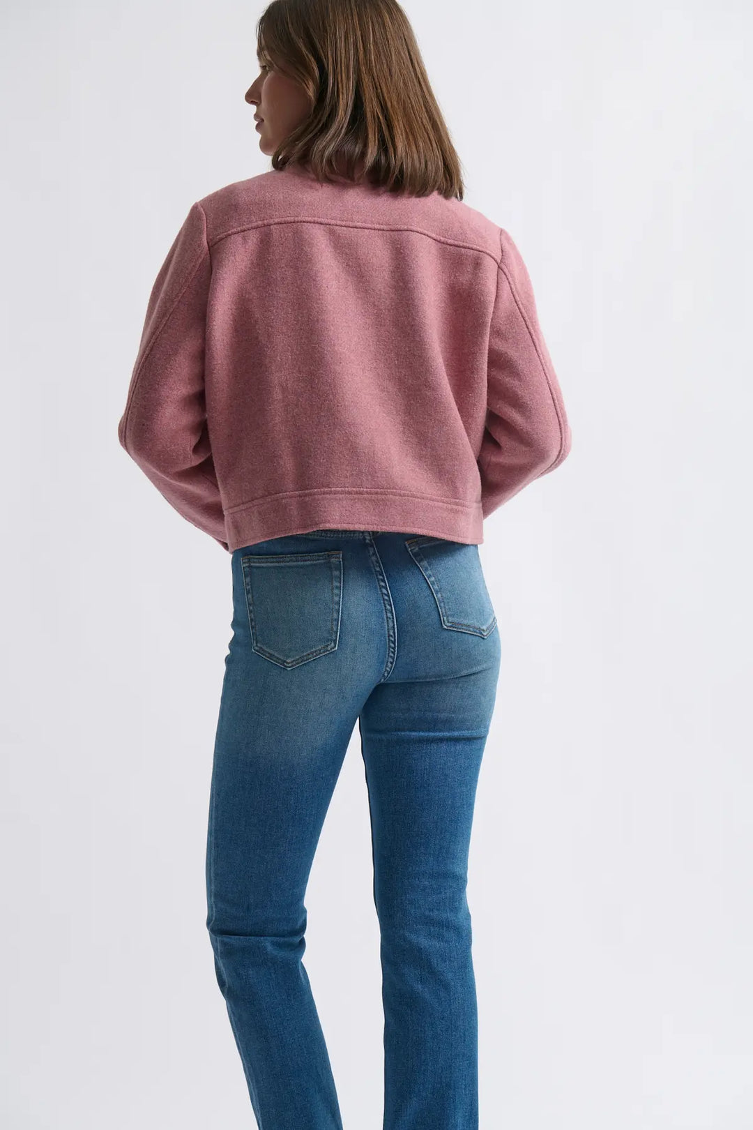 Person wearing a pink jacket and blue jeans on a white background