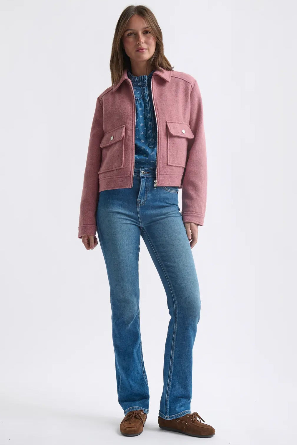 Woman wearing a pink jacket, blue jeans, and brown shoes on a white background