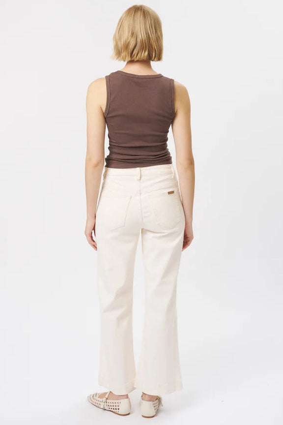 A woman viewed from behind wearing a brown ribbed sleeveless top and off-white wide-leg cropped pants, standing against a plain white studio background.