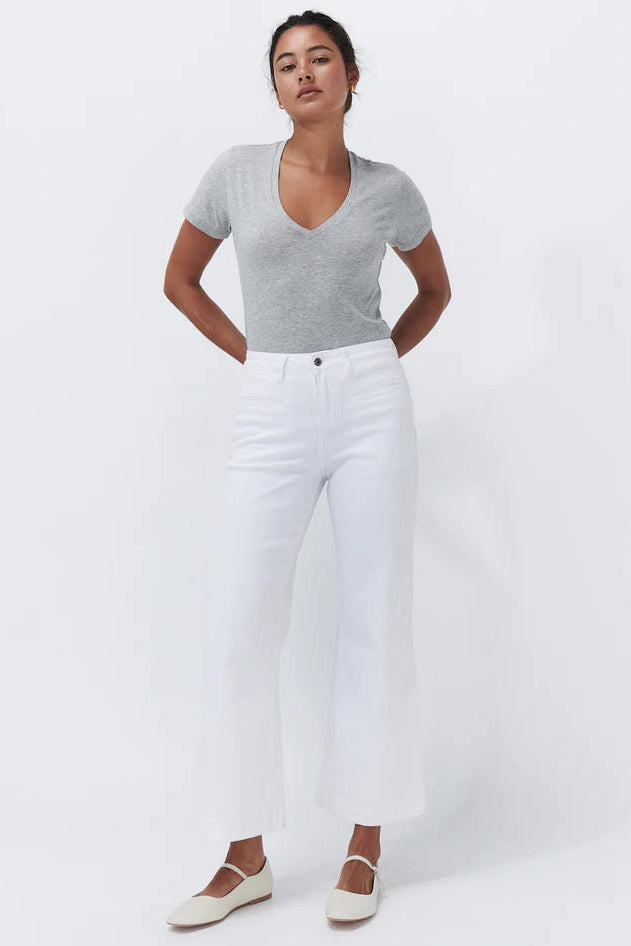 A woman modeling a light gray short-sleeve v-neck top and white cropped wide-leg jeans with white Mary Jane flats, standing against a plain white studio background.