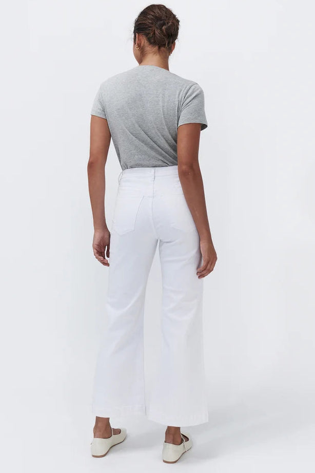 A woman shown from the back wearing a heather gray short-sleeve t-shirt, white wide-leg cropped pants, and off-white slip-on shoes, photographed against a seamless white studio background.