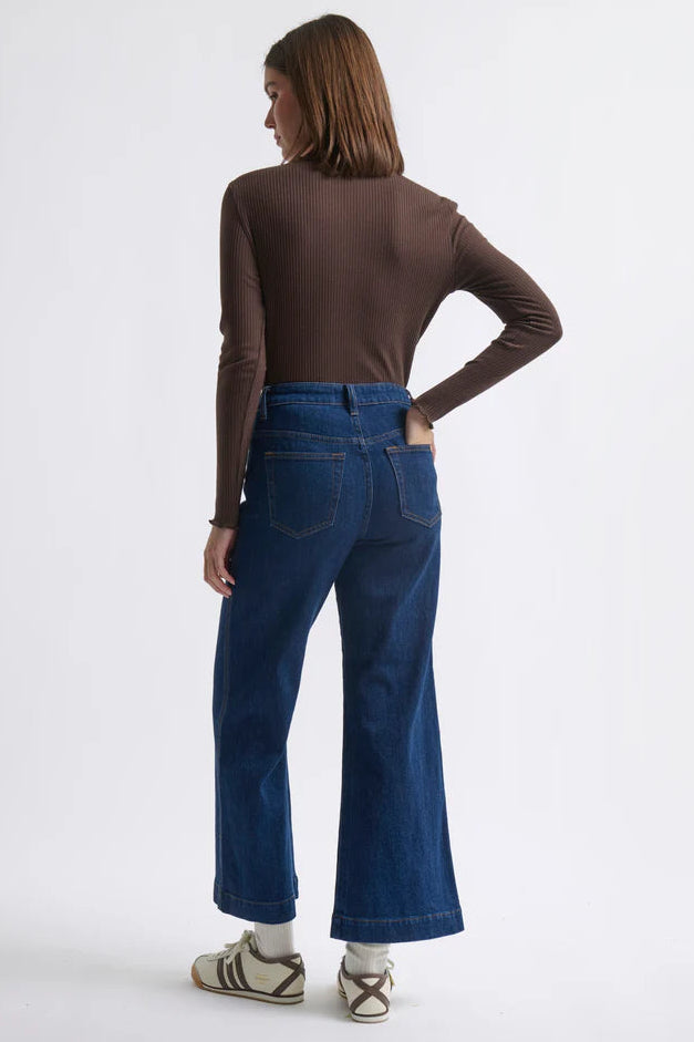 Person wearing blue jeans and a brown long-sleeve top on a white background