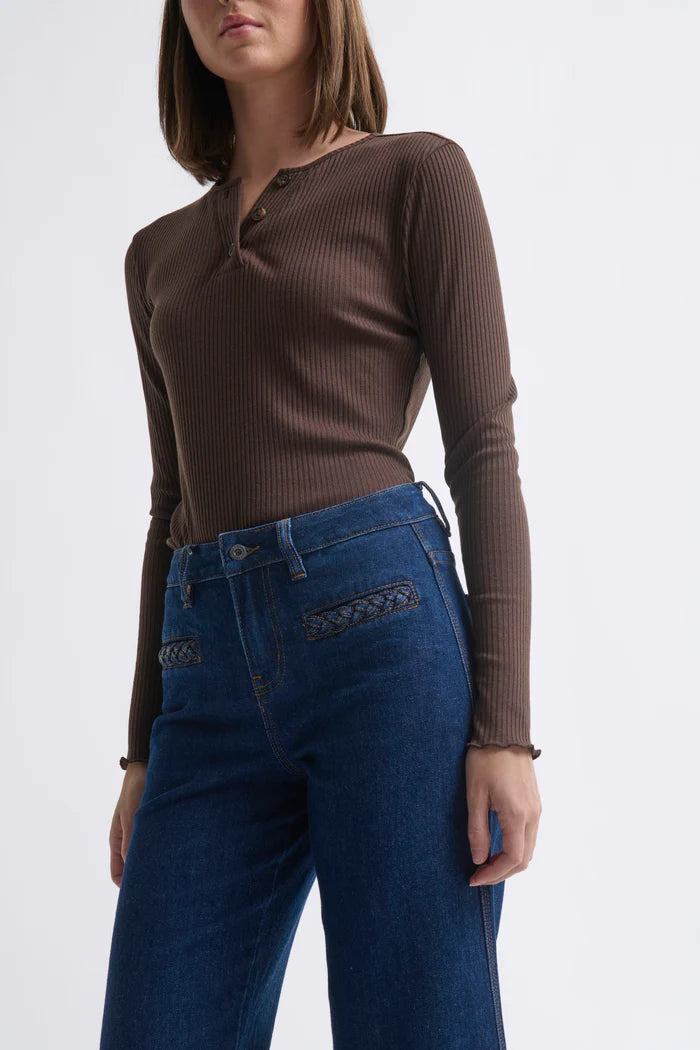Woman wearing a brown ribbed long-sleeve top and blue jeans on a white background