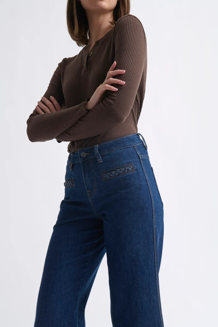 Person wearing a brown long-sleeve top and blue jeans on a white background