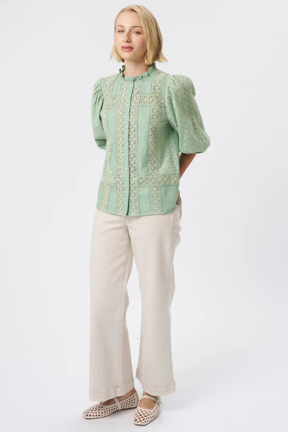 A woman modeling a light green embroidered blouse with puff sleeves and cream wide-leg trousers against a plain white studio background.