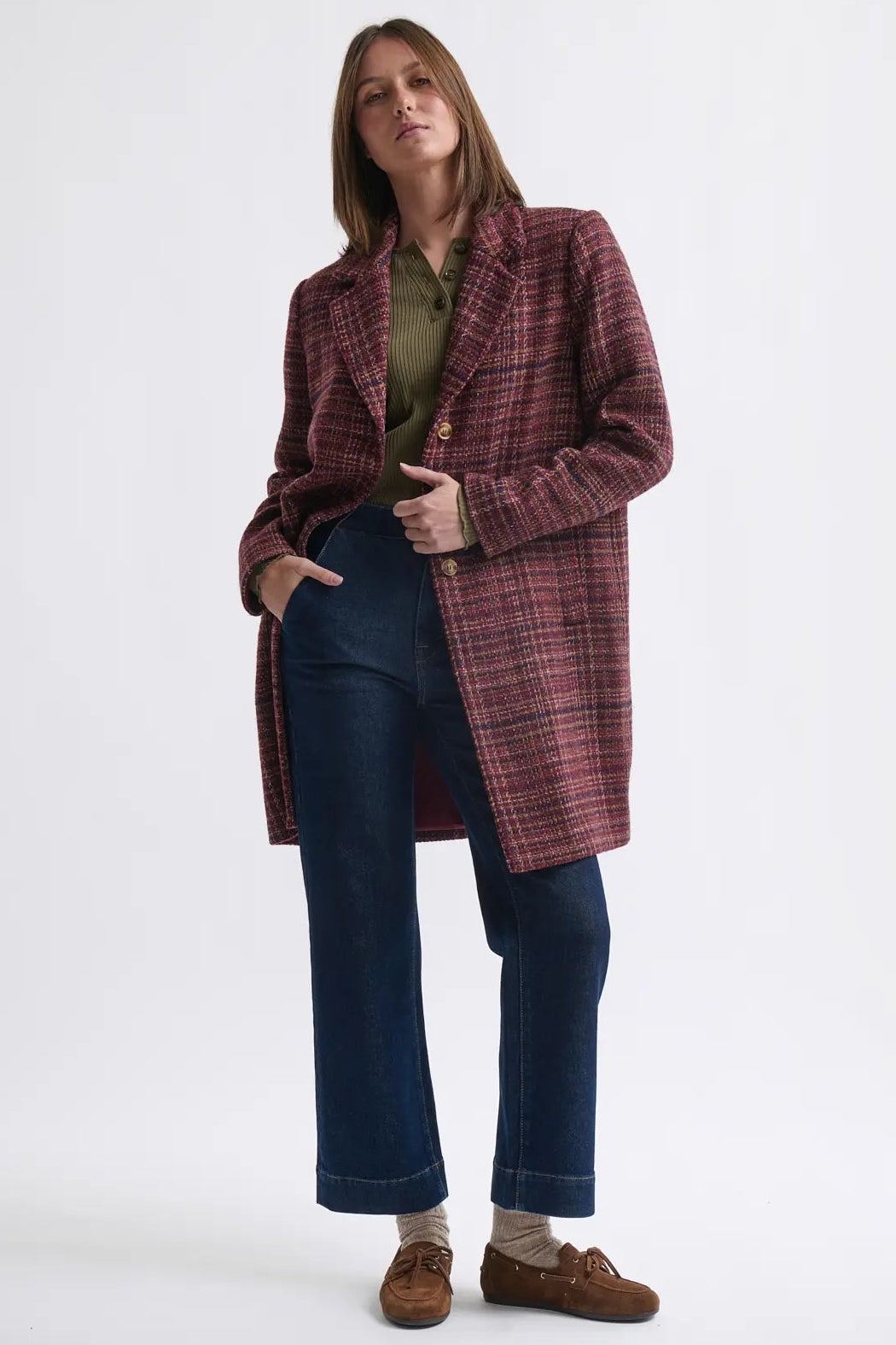 Woman wearing a plaid coat over a green shirt with blue jeans on a white background