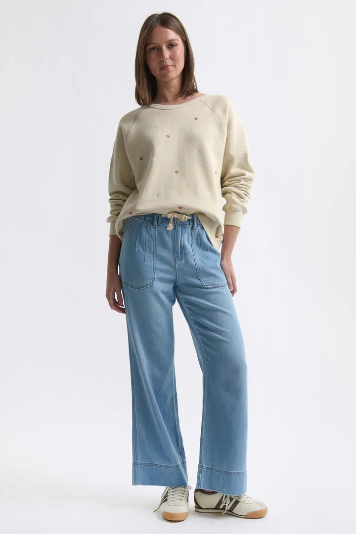 Woman wearing a cream sweater and light blue jeans on a white background