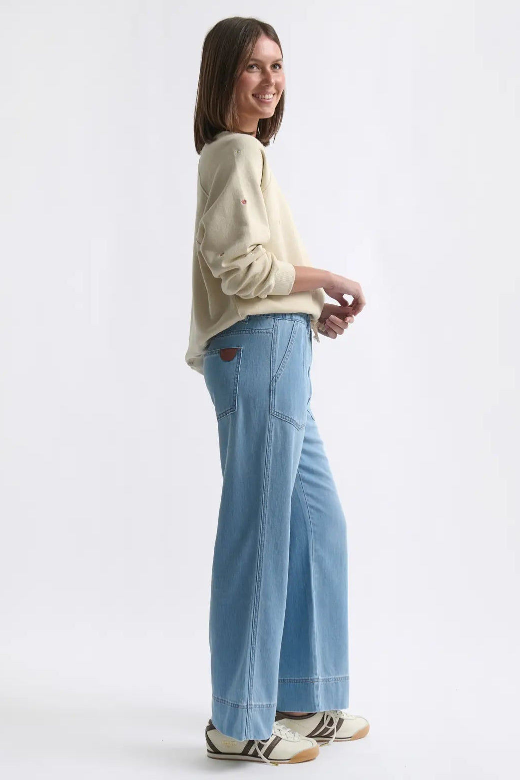 Woman wearing a light-colored sweater and blue jeans on a white background