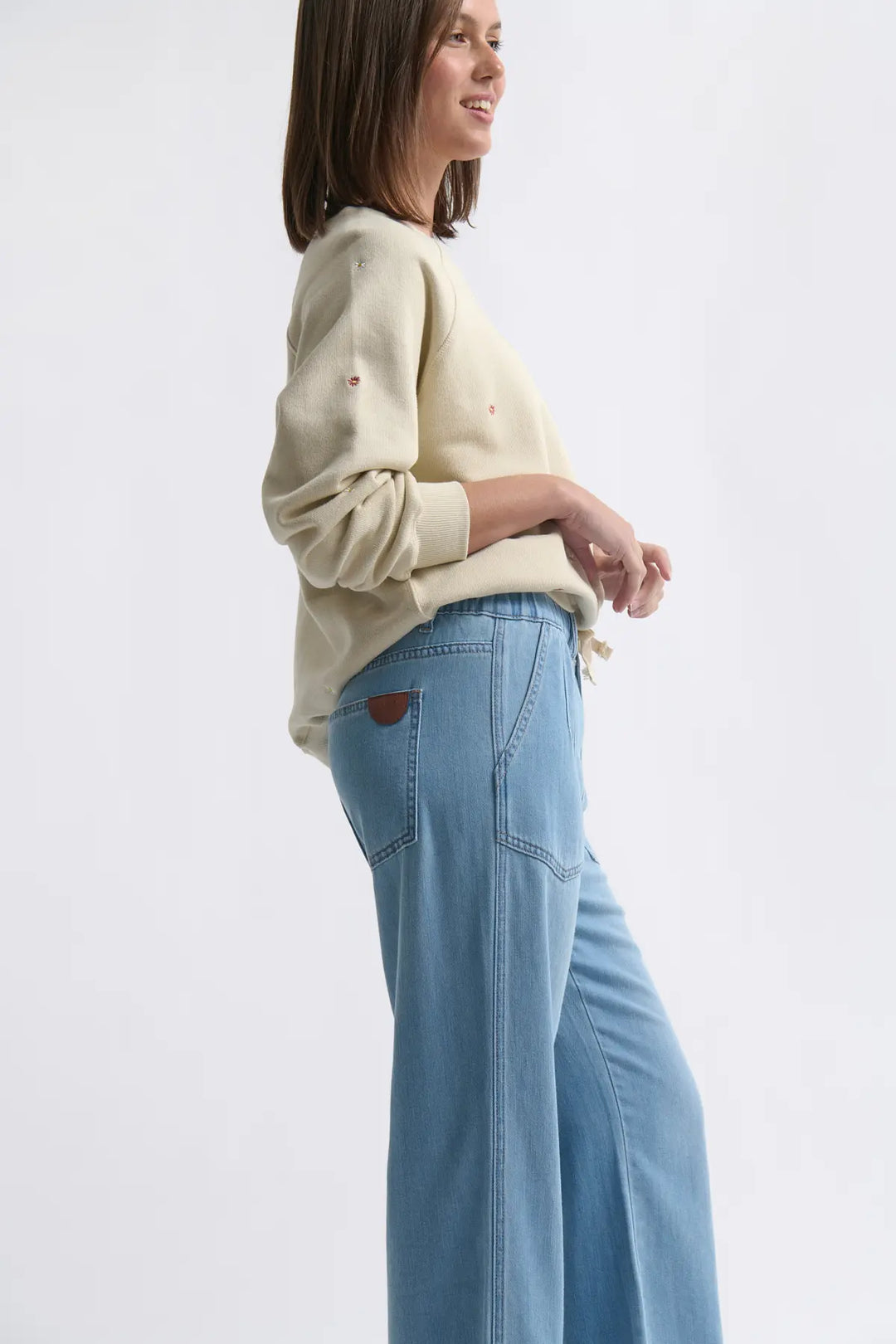 Woman wearing a cream sweater and light blue jeans on a white background