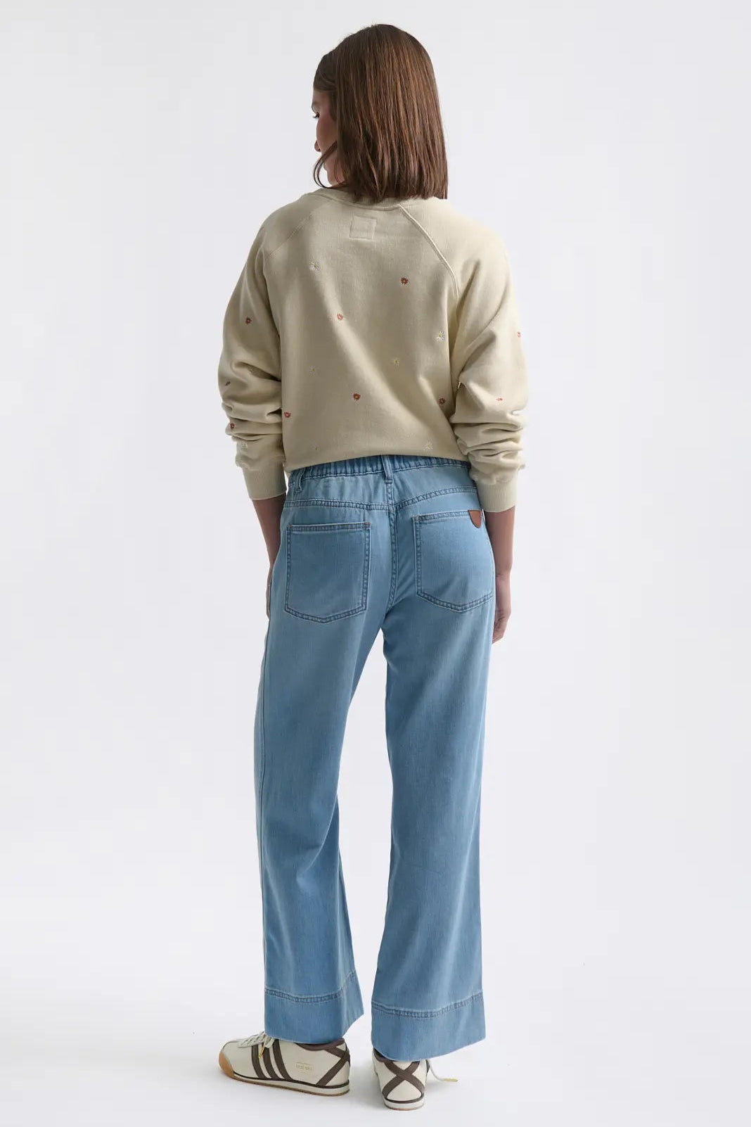 Person wearing a beige sweater and light blue jeans on a white background