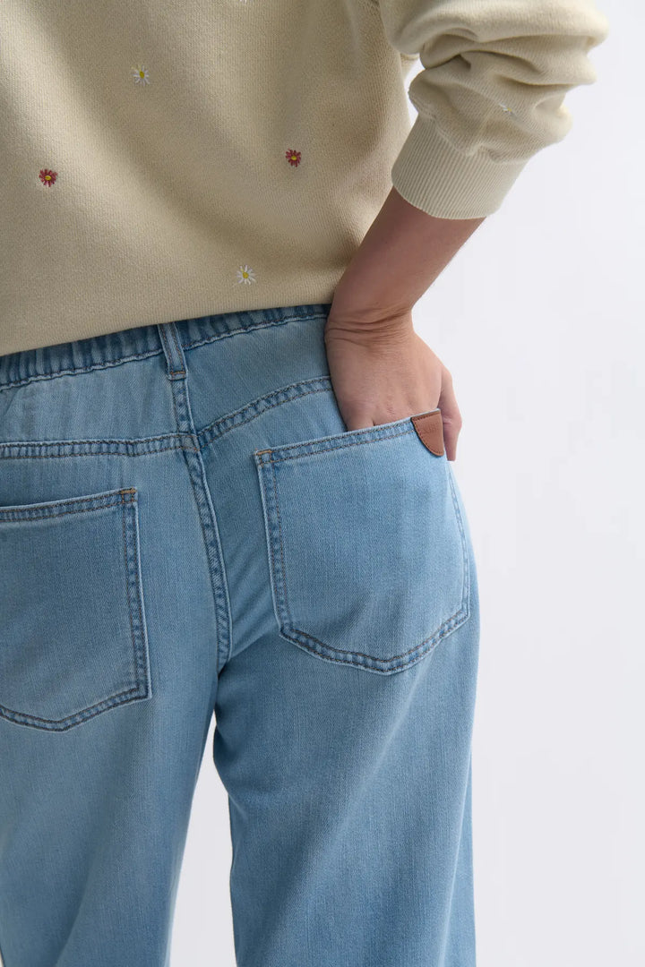 Person wearing light-colored sweater and blue jeans on a plain background