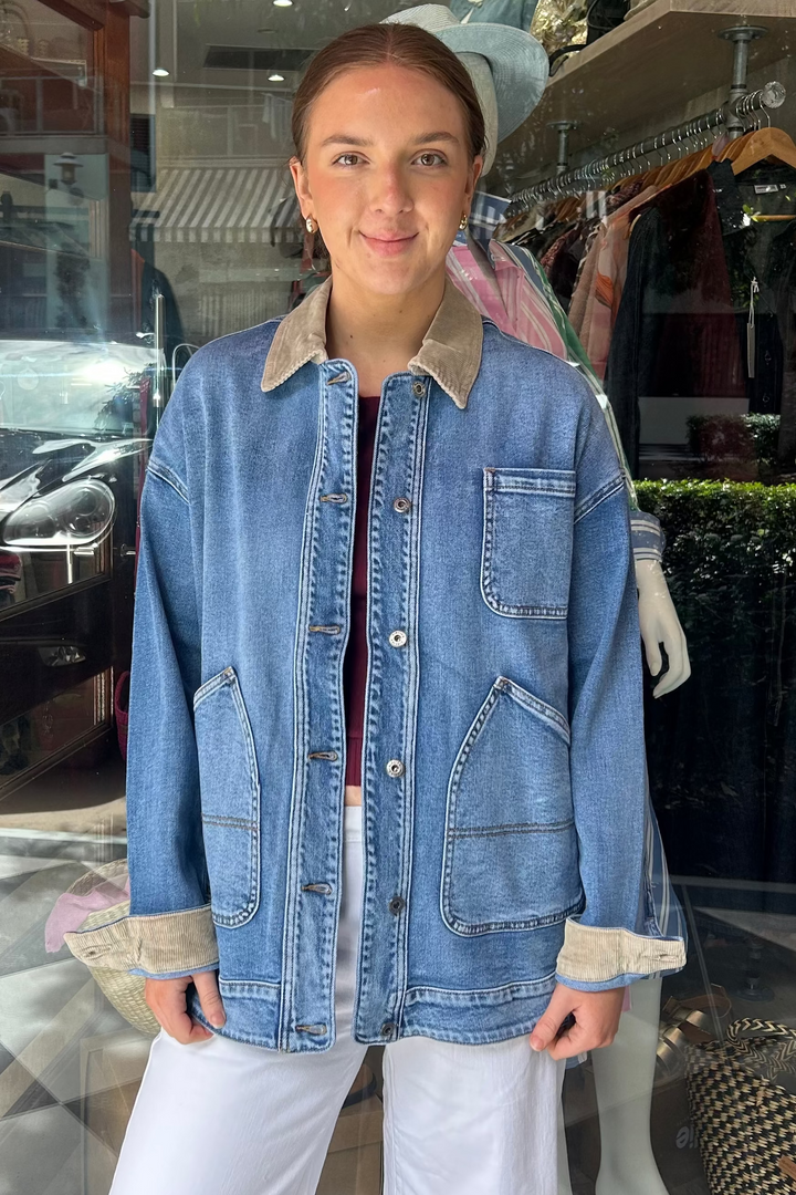 Woman wearing a denim jacket standing in front of a store window display.