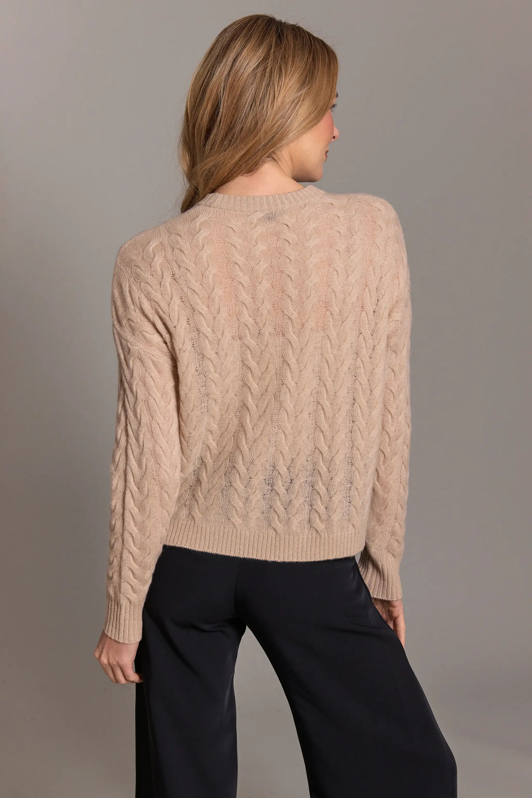 Woman wearing a beige cable knit sweater against a gray background