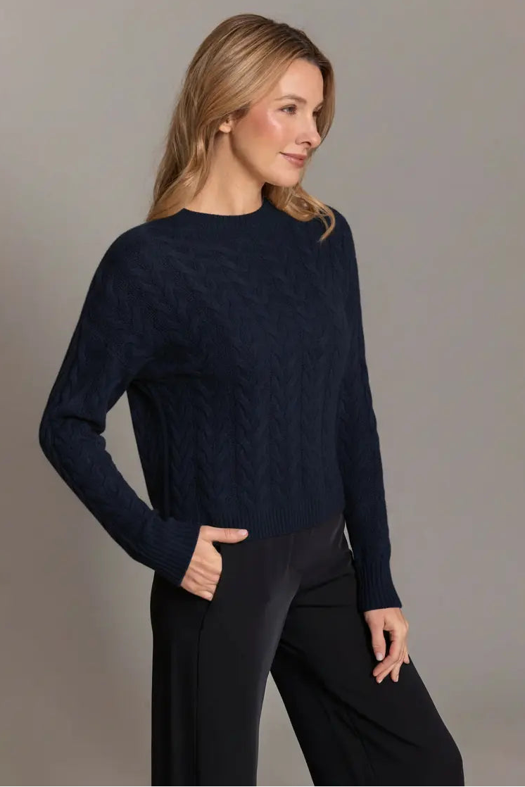 Woman wearing a navy sweater and black pants against a gray background