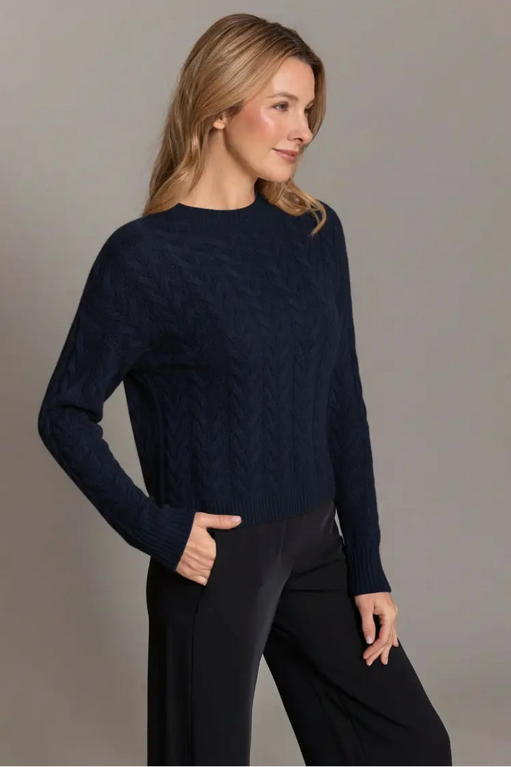 Woman wearing a navy sweater and black pants against a gray background