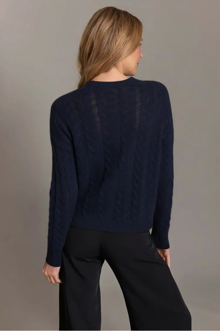 Person wearing a navy sweater and black pants against a gray background