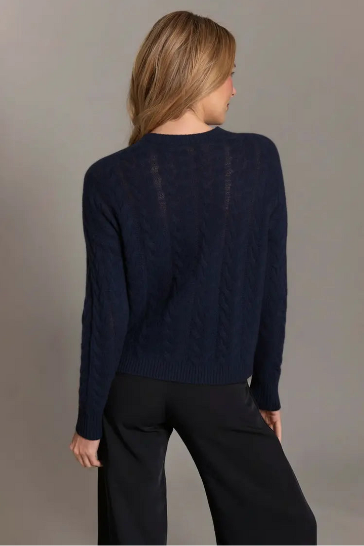 Person wearing a navy sweater and black pants against a gray background