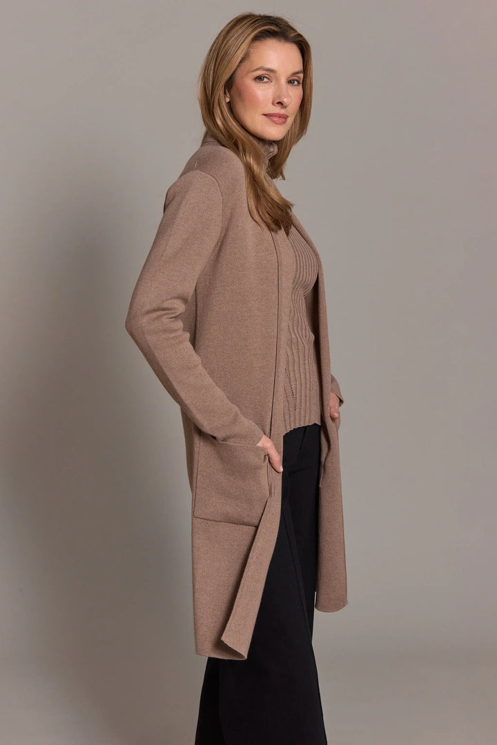 Woman wearing a long beige cardigan against a plain background