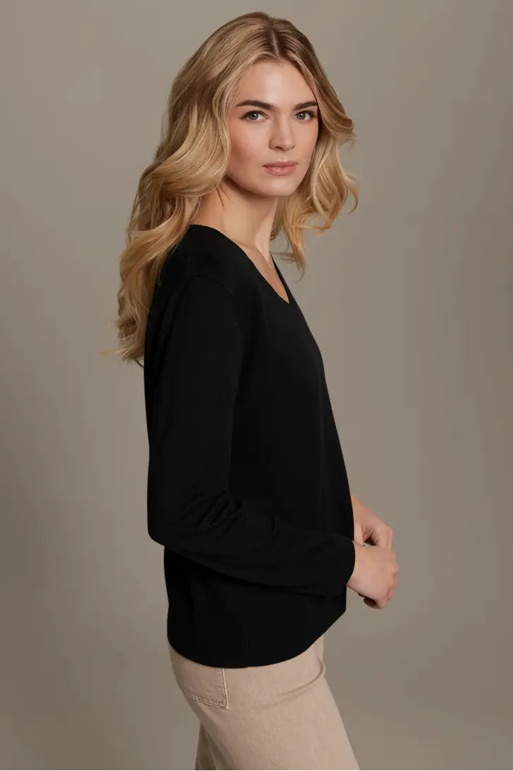 Woman wearing a black top and beige pants against a plain background