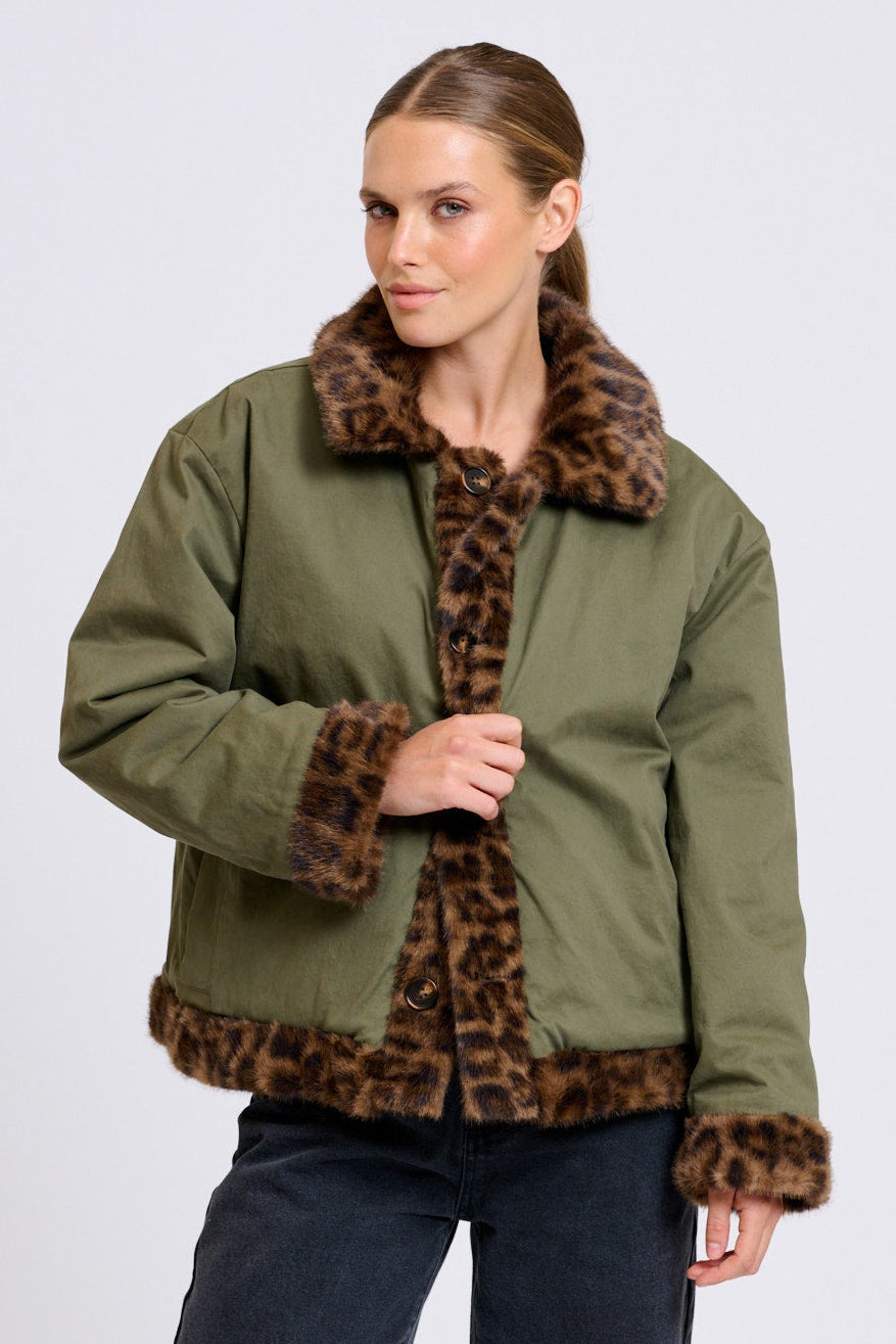 Woman wearing an olive green jacket with leopard print trim on a white background
