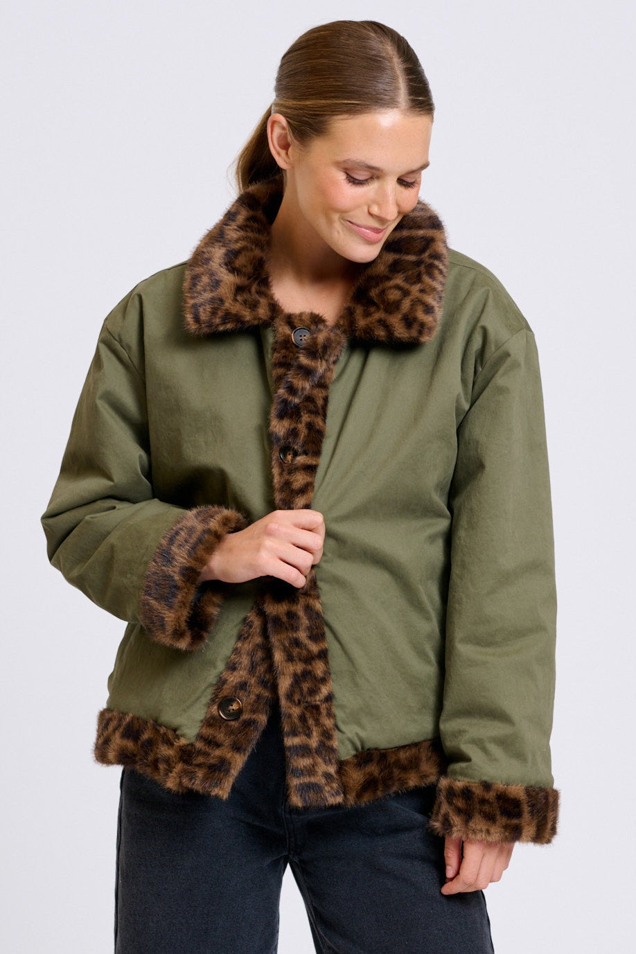 Woman wearing a green jacket with leopard print trim on a white background