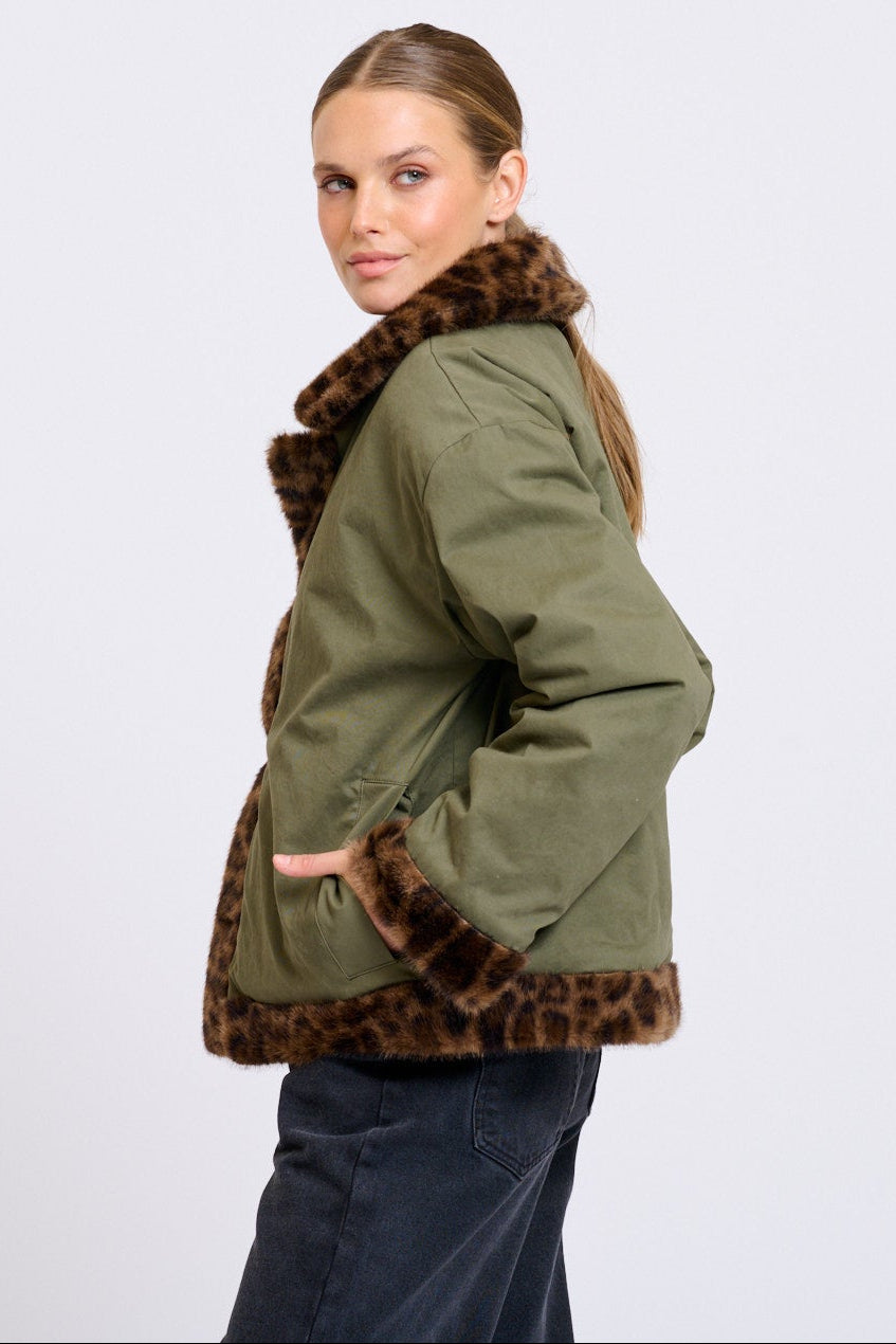 Woman wearing a green jacket with leopard print trim on a white background