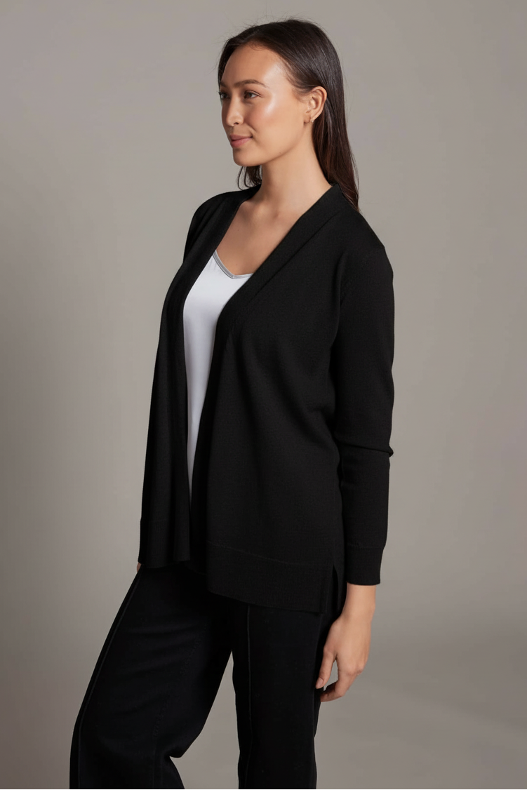 Woman wearing a black cardigan over a white shirt and black pants on a gray background