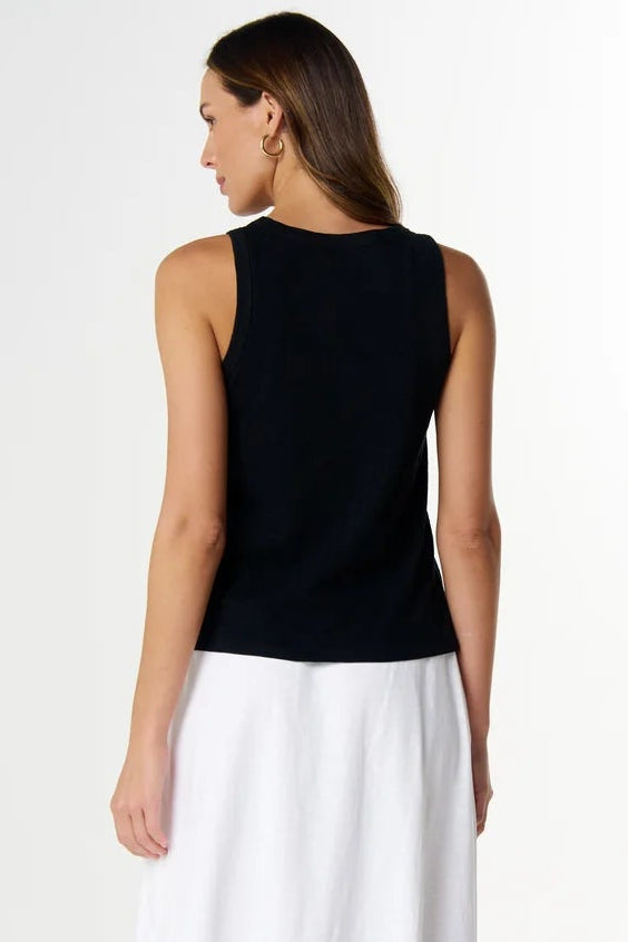 A woman shown from the back wearing a sleeveless black top and a long white skirt, standing against a plain light gray studio background.