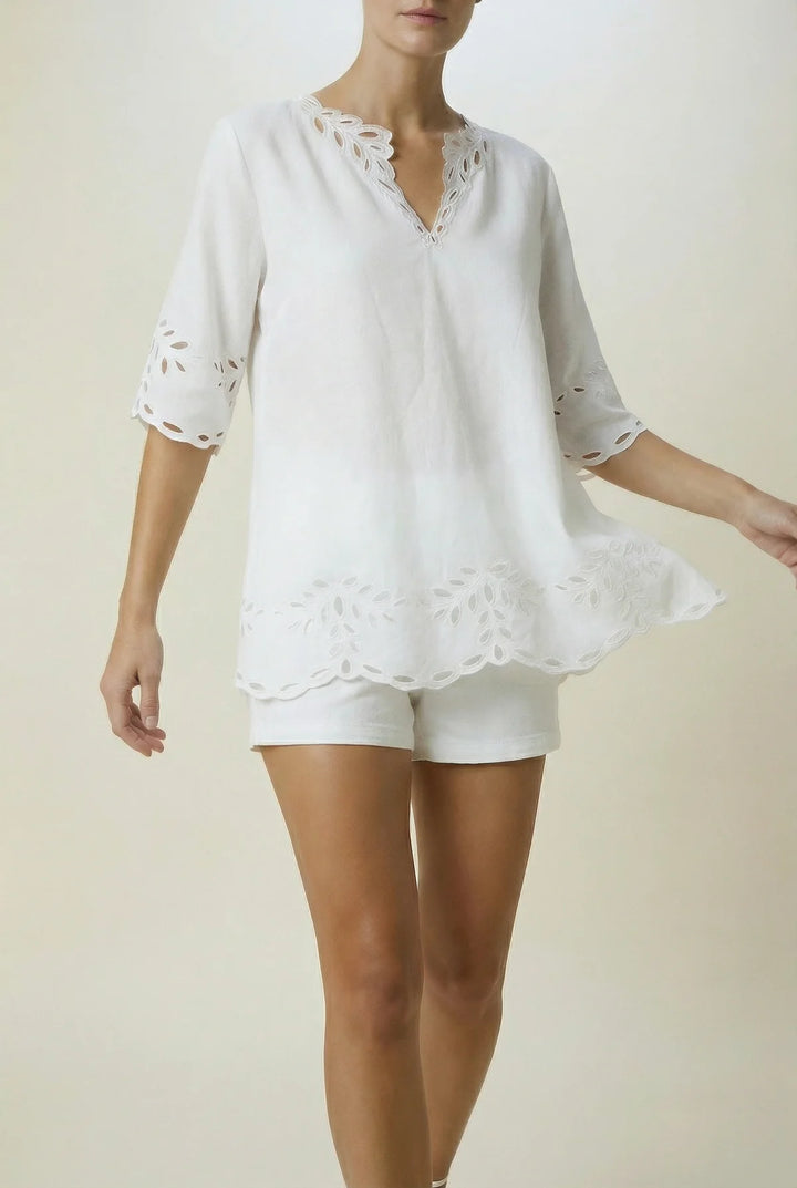 A woman modeling a white eyelet short-sleeve top and matching shorts against a plain beige studio background.